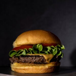 Home Close-up of a delicious cheeseburger with fresh lettuce and tomato against a dark background.