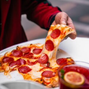 Home Close-up of a hand pulling a cheesy pepperoni pizza slice, perfect for food lovers.