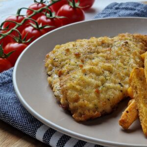 Tasty breaded schnitzel with crispy fries and fresh cherry tomatoes on a wooden table.