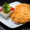 Golden crispy schnitzel served with a fresh vegetable salad, presented on a square plate.