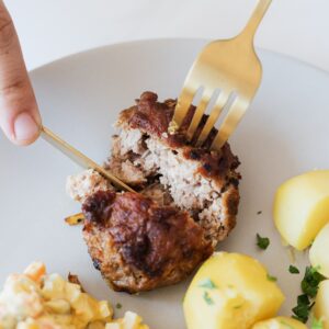 From above of crop faceless person with cutleries cutting tasty homemade fried meat cutlet garnished with boiled potatoes and parsley